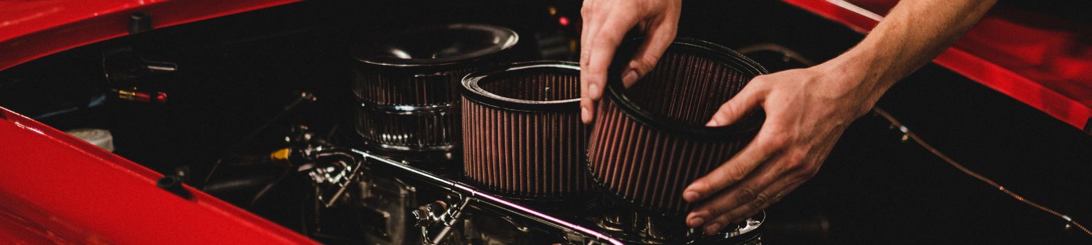Een rond sportfilter wordt in de motorruimte van een rode auto gemonteerd