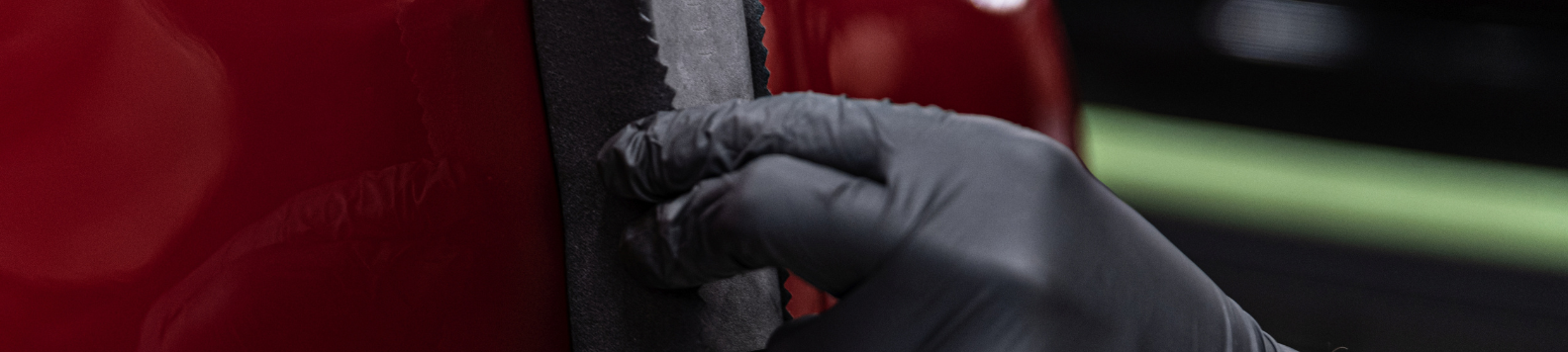 Een gehandschoende hand polijst een rode wagen met een polijstblokje