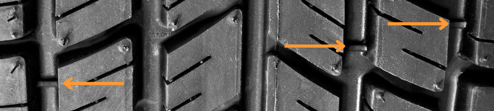Oranje pijlen wijzen de tread wear indicator aan in het profiel van een nieuwe autoband